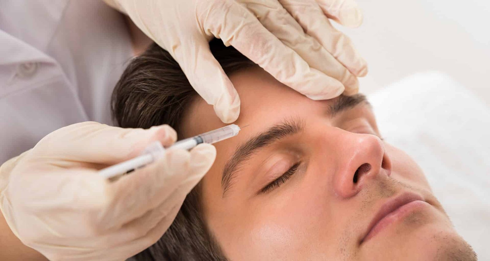 Un professionnel administrant une injection sur le front d'un homme allongé, les yeux fermés, dans un environnement de soins esthétiques.