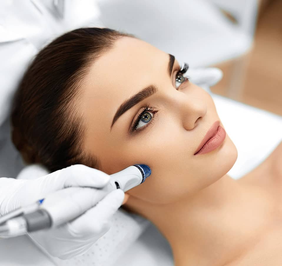 Une femme recevant un traitement facial avec un appareil, montrant un professionnel en soins de la peau. La scène met en avant des détails sur le visage et la technologie utilisée pour le soin. Hydrafacial Paris.